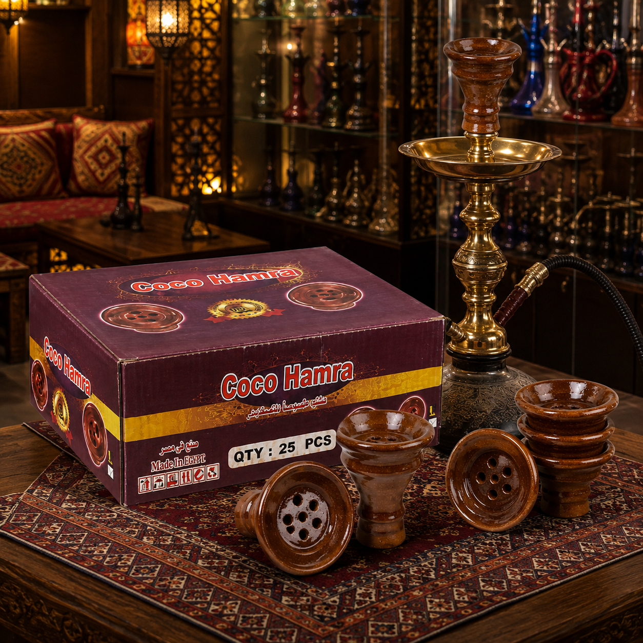 A boxed set of Coco Hamra hookah accessories displayed in a warm, ornate shop setting. The set includes a purple and gold box labeled &